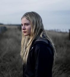 a woman with long blonde hair standing in a field