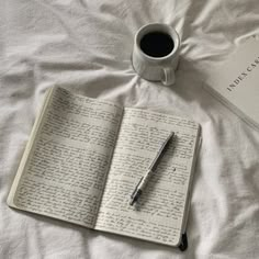 a cup of coffee and an open book on top of a bed with writing in it