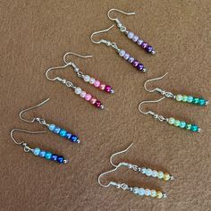 six different colored beads are hanging from silver earwires on a brown carpeted surface