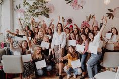 a group of women holding up papers in front of a wall with flowers on it