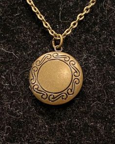 a gold locke necklace with a chain around it on a black surface, the pendant has an ornate design