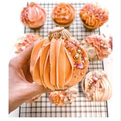 a person holding up a pumpkin shaped cupcake