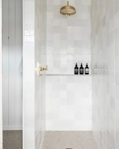 a white tiled bathroom with gold fixtures and toiletries on the wall, next to a shower head