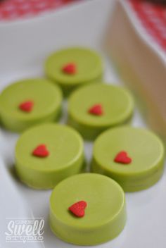 small green and red cakes with hearts on them sitting on a white plate, ready to be eaten