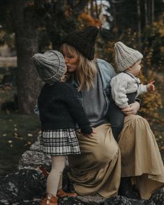 a woman sitting on top of a rock holding a baby in her lap and wearing a hat