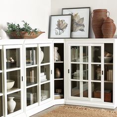 a white cabinet with glass doors and some vases on the top shelf next to it