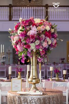 a tall gold vase filled with pink and white flowers on top of a round table