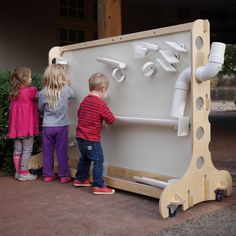 two children are playing with a water fountain made out of wood and pipe fittings