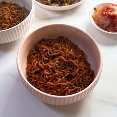 three bowls filled with food on top of a white countertop next to other dishes