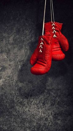 two red boxing gloves hanging from strings against a dark background with only one pair left