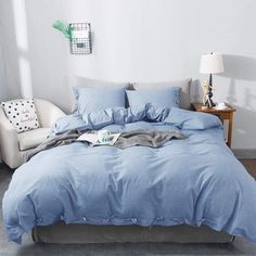 a bed with blue sheets and pillows in a white room next to a lamp on a table