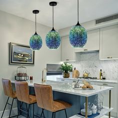 three lights hanging from the ceiling above a kitchen island with marble counter tops and stools