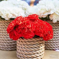 red and white carnations are in baskets on a table with rope wrapped around them