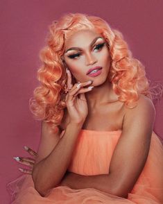 a woman with bright pink hair and makeup posing for a photo in an orange dress