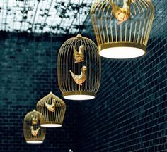 three gold birds in cages hanging from the ceiling and some lights above them are lit up