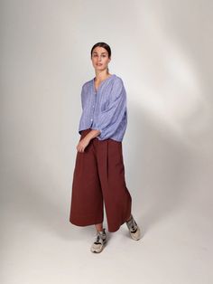 a woman standing in front of a white background wearing brown pants and a blue shirt