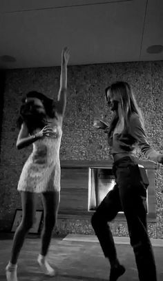 two young women are dancing in an empty room, one is holding her hand up