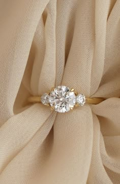 an engagement ring with three stones on top of it, sitting on a beige cloth