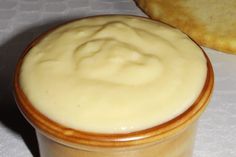 a container filled with cream sitting on top of a table next to a piece of bread