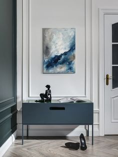 a painting is hanging on the wall next to a table with a pair of black shoes