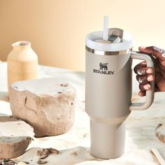 a person holding a coffee cup in front of some wood shavings on a table