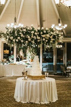 a wedding cake sitting on top of a table under a chandelier filled with flowers