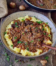 a bowl filled with mashed potatoes covered in sausage and lentils on top of a wooden table