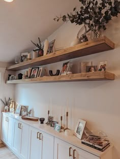 two wooden shelves with pictures on them above a white cabinet and sideboard in a living room