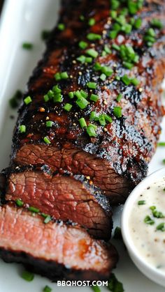 steak with sauce and chives on a white platter next to a small bowl