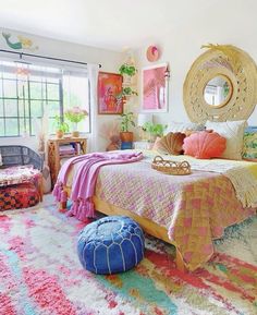 a bedroom decorated in pink, yellow and blue with a large round mirror above the bed