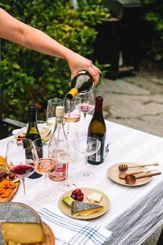 a person pours wine into glasses on a table with cheese, crackers and bread