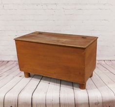 an old wooden box sitting on top of a white striped tableclothed floor next to a brick wall