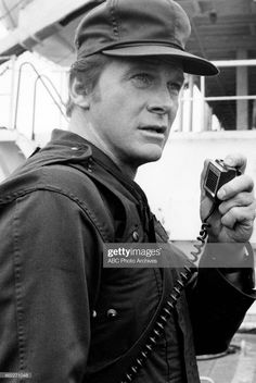 a man wearing a hat and holding a cell phone in his hand while standing on the deck of a ship