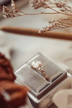 an engagement ring sitting on top of a silver box next to some dried flowers and branches