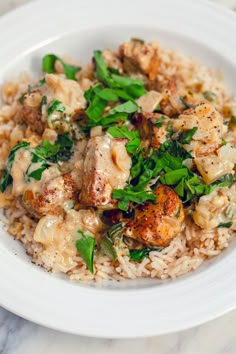 a white plate topped with rice and meat covered in sauce on top of a marble table