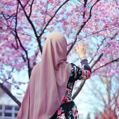 a woman in a hijab standing under a tree with pink flowers