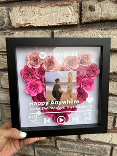 a person holding up a framed photo with pink flowers in the shape of a heart