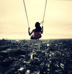 a woman is swinging on a swing in the air with cityscape in the background