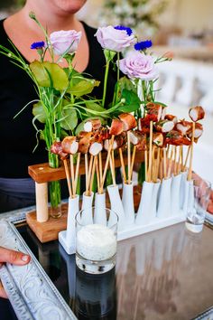 a tray with skewered meats and flowers on it next to a woman