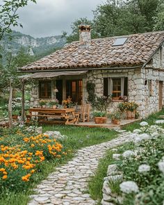 a small stone house with flowers in the foreground and a path leading to it