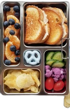 an open lunch box with fruit, vegetables and bread in it on a white background