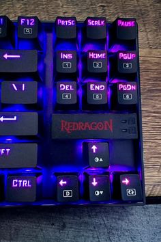 a close up of a keyboard on a wooden surface with blue lights and the words redragon printed on it