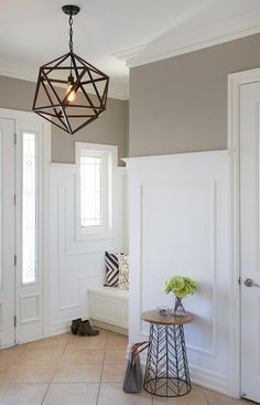 an entryway with a table, vase and lamp hanging from it's ceiling