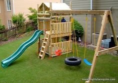 a wooden swing set with a slide and swings on the grass in front of a house