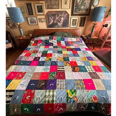 a bed covered in lots of colorful quilts next to lamps and pictures on the wall