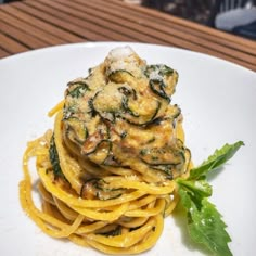 a white plate topped with pasta covered in cheese and spinach sauce next to a leafy green garnish