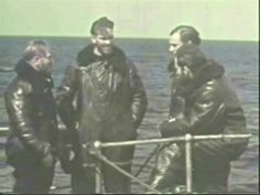 three men standing on the deck of a ship talking to each other while another man watches