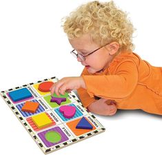 a toddler playing with a puzzle board on the floor, while wearing glasses and an orange shirt