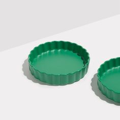 two green pie pans sitting on top of a white table next to each other