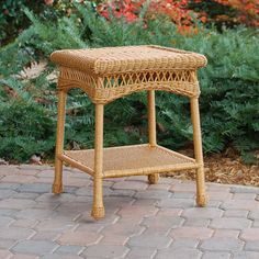 a wicker side table on brick walkway next to bushes and flowers in the background